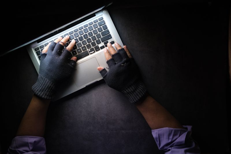 Gloved hacker with hands on laptop keyboard