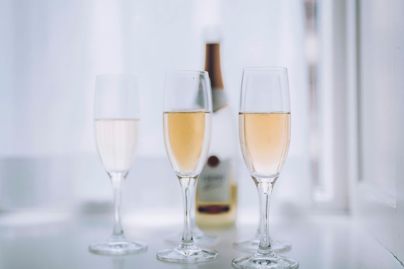 Three glasses of sparkling white wine, with a bottle of wine blurred in the background.