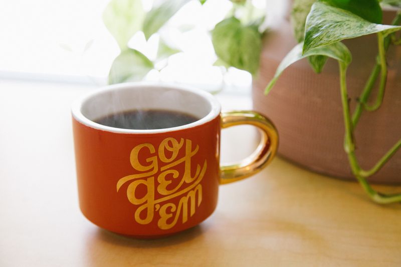 A coffee mug on a table. The mug has the words 'Go Get 'Em' painted on the side.