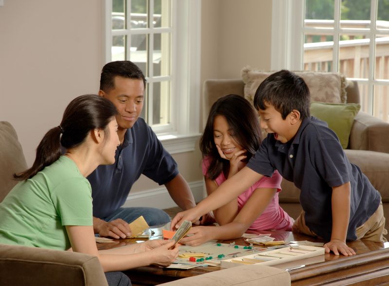 An Asian family made up of adults and children play a board game together.