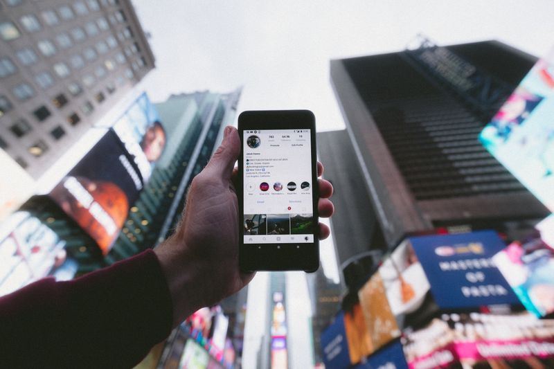 Cell phone screen showing an Instagram profile being help up by a man.