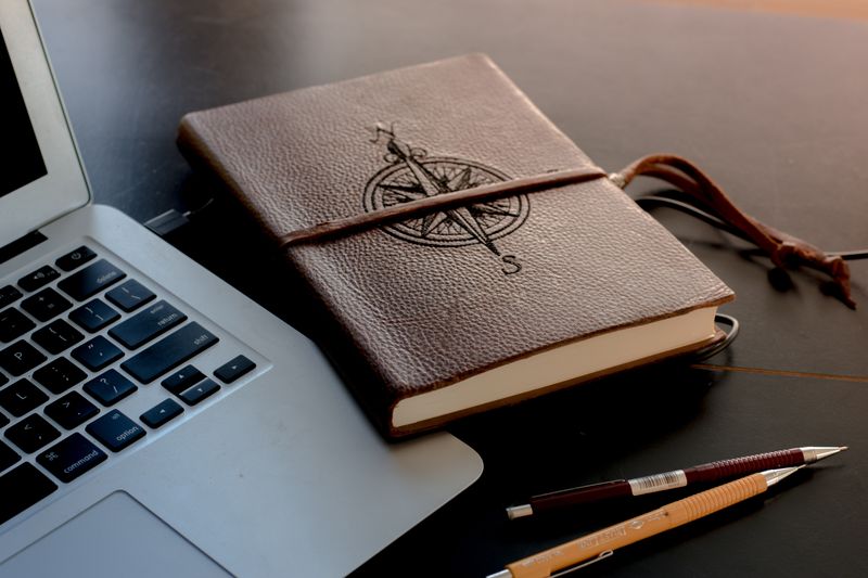 A image showing laptop and a notebook with two pens.