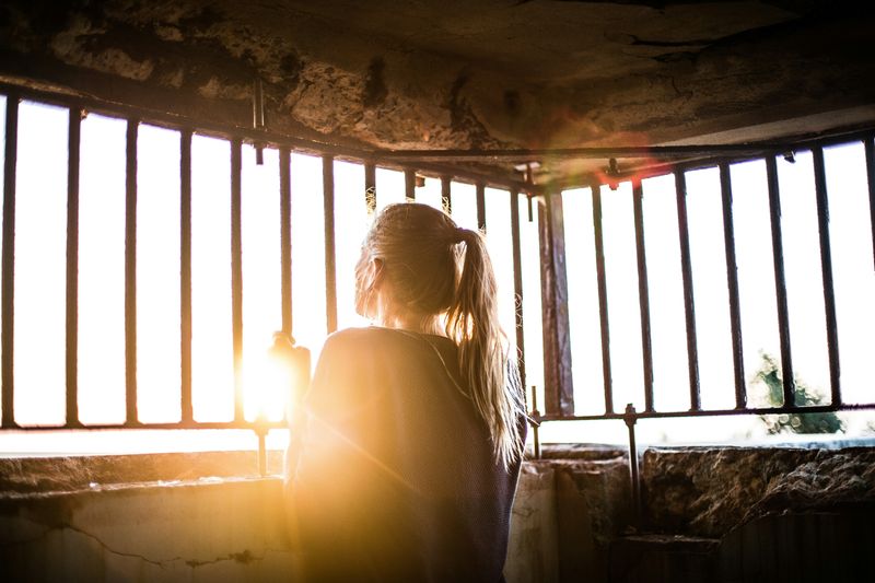 A person standing in a cage looking out, appearing trapped.
