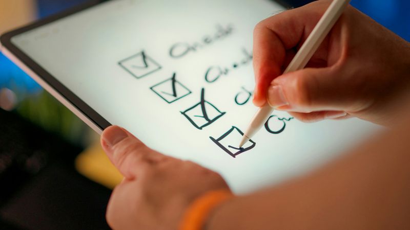 A person using a stylus to check off items on a digital tablet checklist.