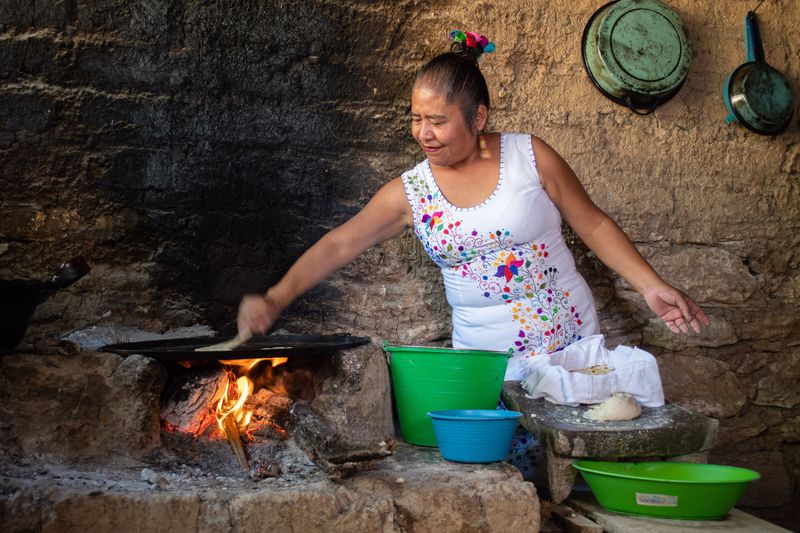 Older Mexican woman cooking tortillas over a fire