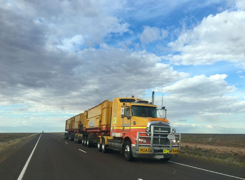 A yellow truck driving under a cloudy sky.