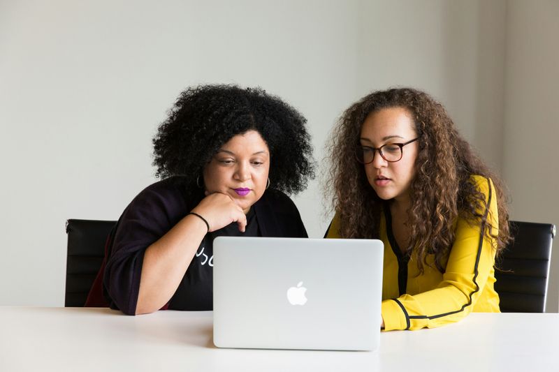 A teacher and staff member working on one laptop together.