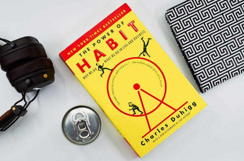 Charles Duhugg's The Power of Habit on a desk beside a notebook, a set of headphones, and a drink can.