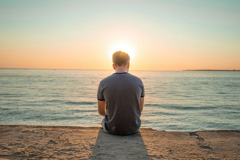 A man sits on a beach watching the sunset. 