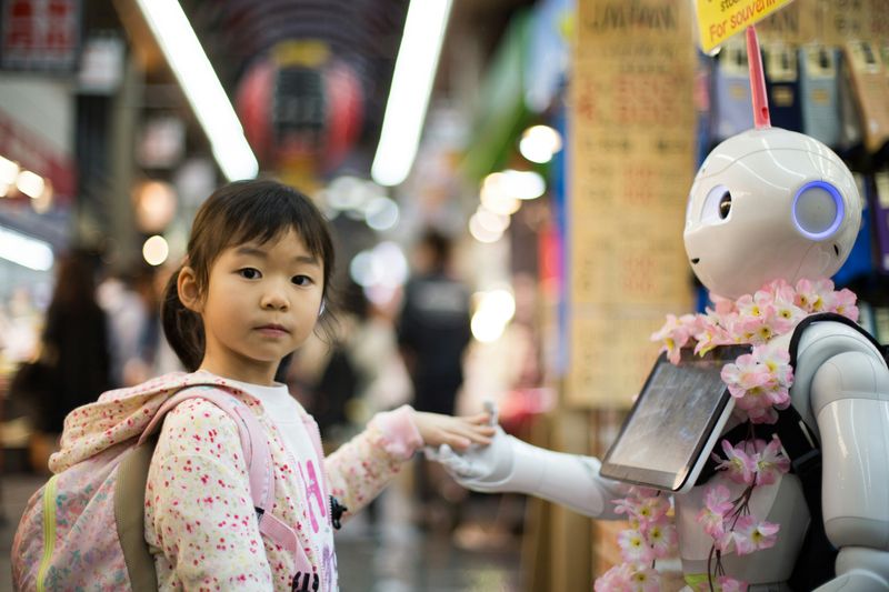 A young girl holding hands with a robot that has a digital tablet on its chest.