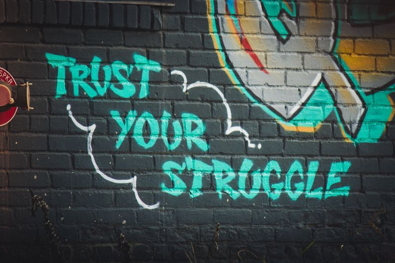 street art on a brick wall that reads "trust your struggle"