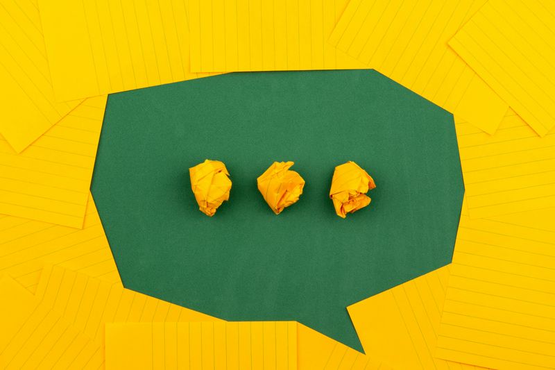 A yellow background with a green speech bubble. The green speech bubble has three yellow dots.