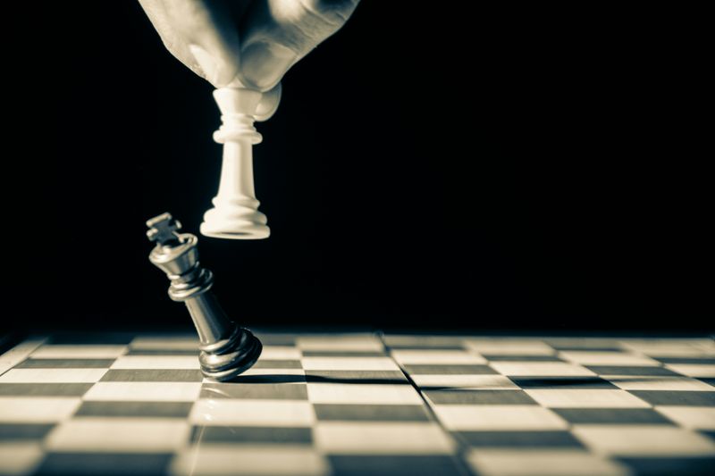 A person knocking over a king in a chess game.