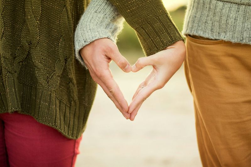 Two people in sweaters forming a heart with their hands by their sides
