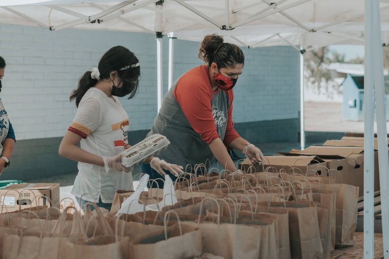 Two women volunteering to pack brown paper bags with food.