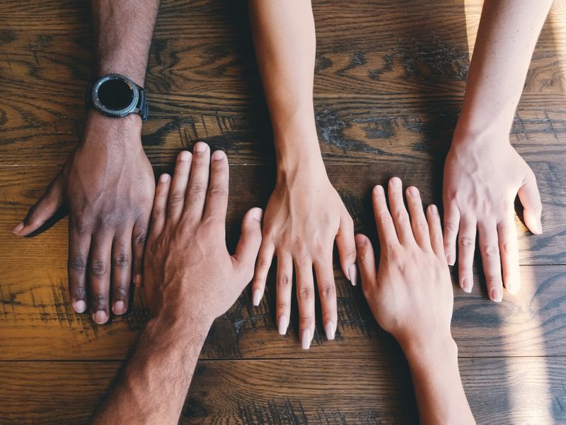 Hands of a diverse group of people spread across a wooden table.