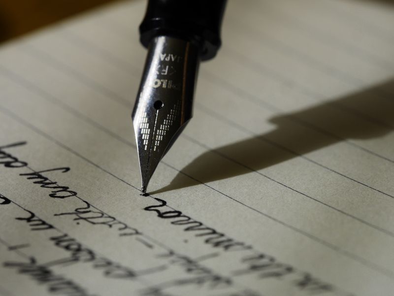 a close up shot of a fountain pen writing on a lined piece of paper 