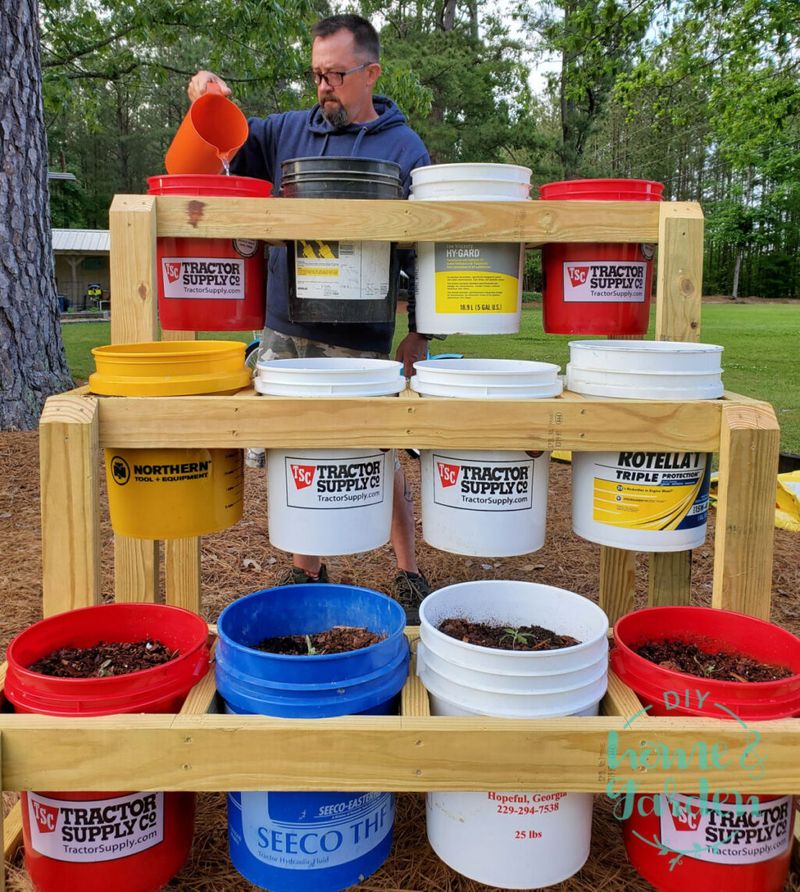A person watering plants in a bucket garden stand.