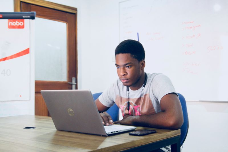 Young man sits at a desk in a college classroom with his computer in front of him.