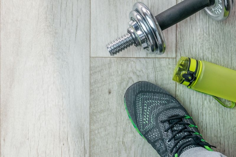 Sneakers, a water bottle, and dumbbells on a gym floor.