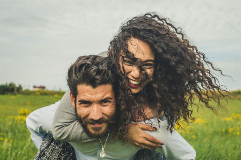 A man and woman in a field. The man carries the woman on his back.