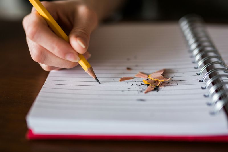 A person writing in a notebook with a pencil.