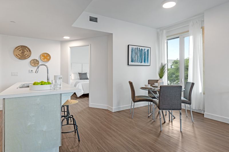 A neat and sparse apartment is pictured with neutral furniture, a white kitchen island and white walls