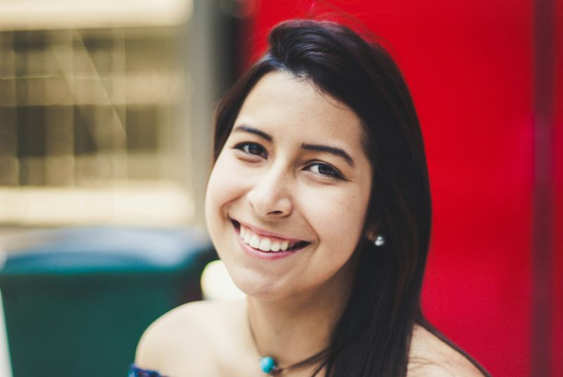 A woman with dark brown hair smiling, wearing a turquoise necklace.