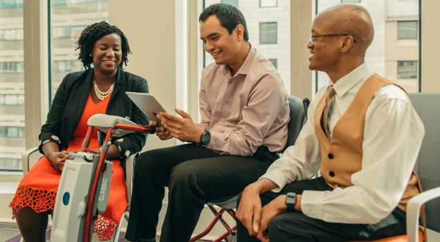 Three people in an office. One person uses a mobile assistive device.