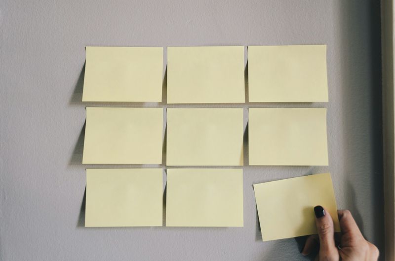 A series of sticky notes on a wall. A hand removes one note.