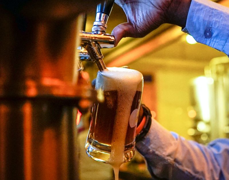A bartender pours beer from the tap. The foam from the beer is spilling over the side of the mug.