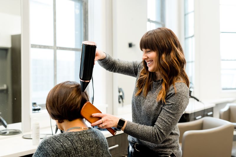 Hairstylist styling a woman's hair.  Photo by Adam Winger on Unsplash