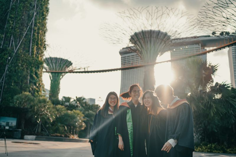 Four graduates in academic gowns smiling together outdoors.