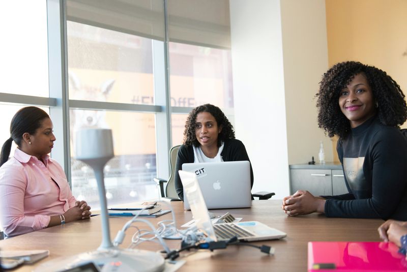 Three women talking in an office setting. One is happily smiling.