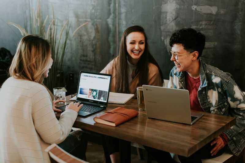 three people laughing at a table with their laptops
