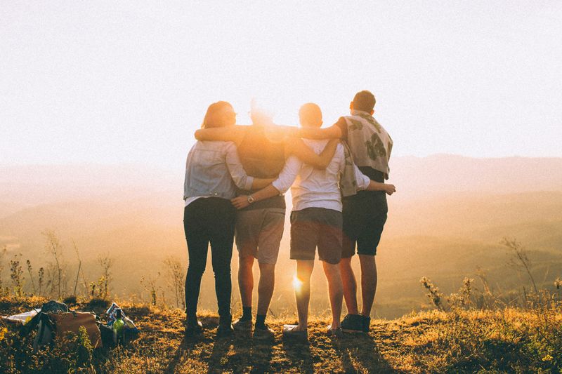 Four people at the top of a mountain facing the sunrise with their arms around each other. 