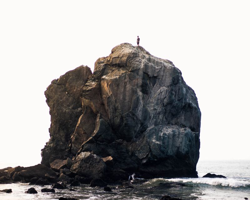 A person on top of a giant rock by the ocean.