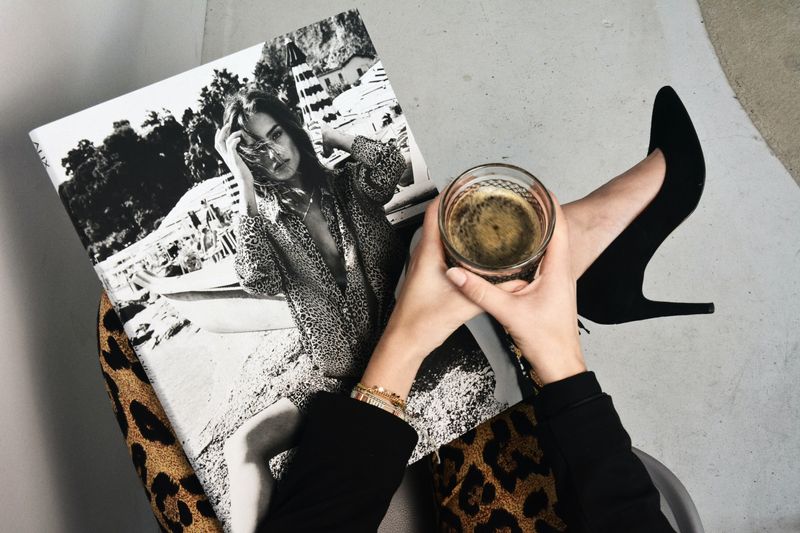 An unidentified woman seated with a cup of coffee and a fashion magazine.