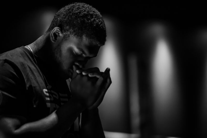 A person with their head bowed down, their eyes closed, their hand's cupped to their face, looking anxious in deep thought.