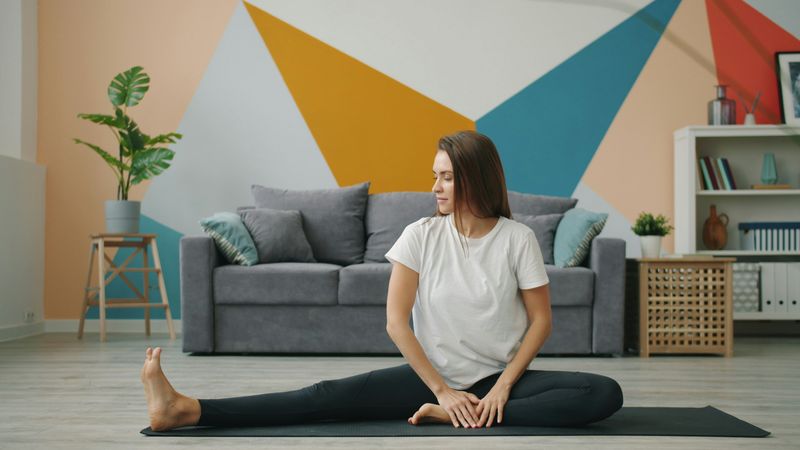 Woman sitting on a yoga mat while stretching her legs.