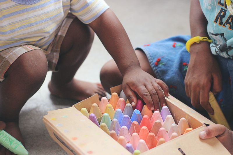 Two children playing with a box of colored chalk