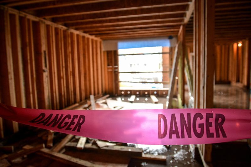 Construction site with exposed wooden framing and a bright pink caution tape labeled “Danger