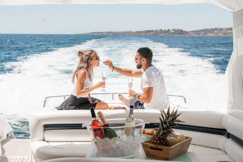 Image: Two people sitting on a yacht with wine and fruit