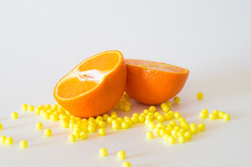 A sliced orange on a table. Small yellow balls are spread around the table to represent vitamins and nutrients.