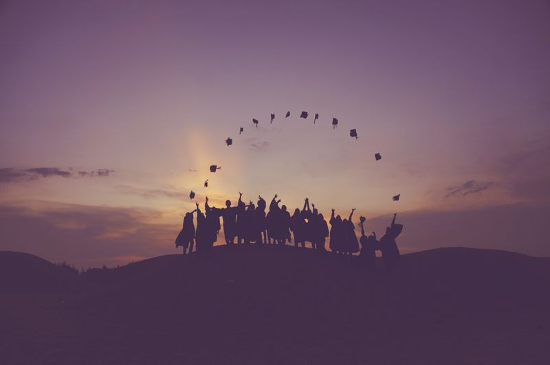 Shadowed figures of young adults throwing their caps in the air to form a semi circle. 