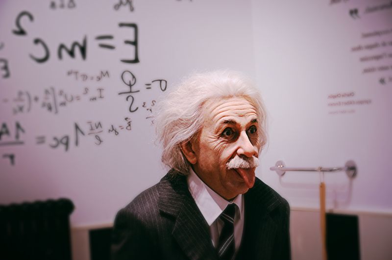 A wax statues of Albert Einstein sticking out his tongue in front of a chalkboard covered in equations.