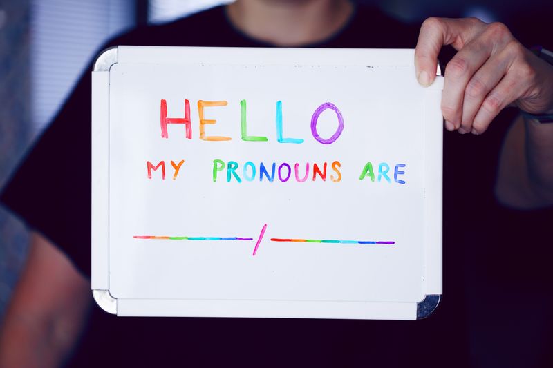 Person holding whiteboard with 'Hello my pronouns are blank/blank