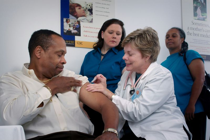 A doctor giving a shot to a patient at a community health centre, with two nurses looking over.