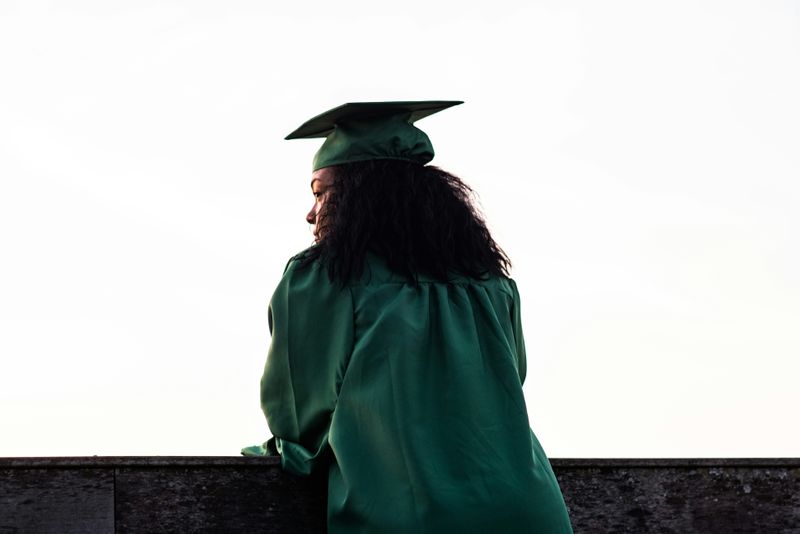 A woman in a graduation cap and gown looking out over the horizon from a balcony.