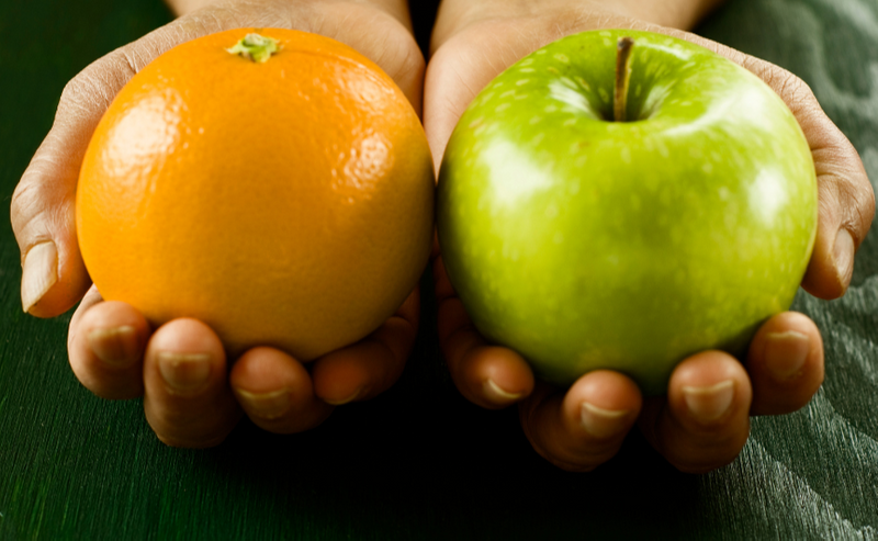 Hands holding an orange and a green apple